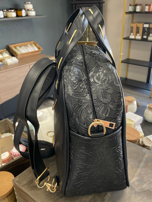 Black leather backpack with floral patterns on a counter in a store setting