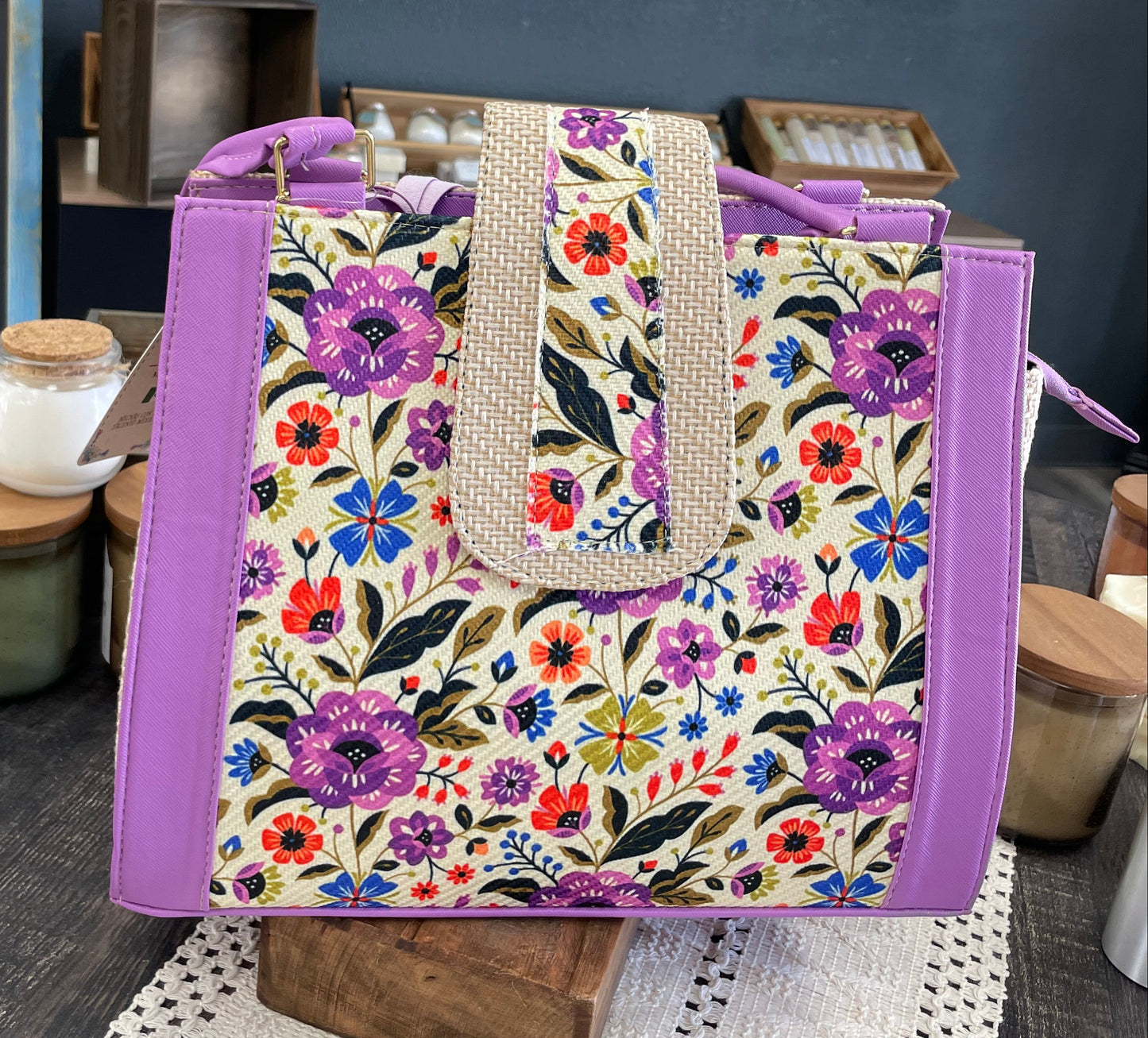 Floral tote bag with purple accents on a wooden stand against a shelf with jars.