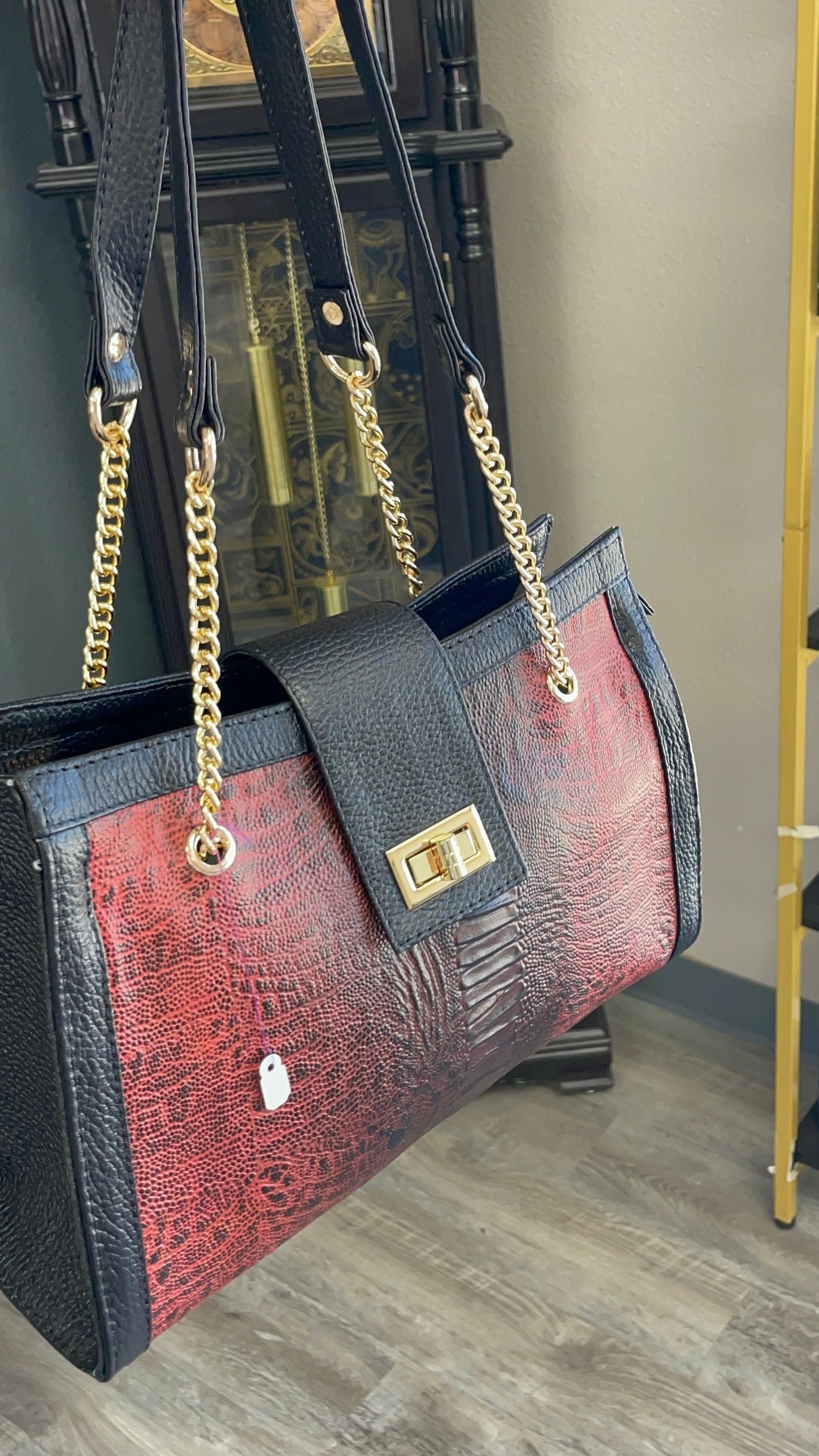 Black and red handbag with gold chain strap held by a person indoors.